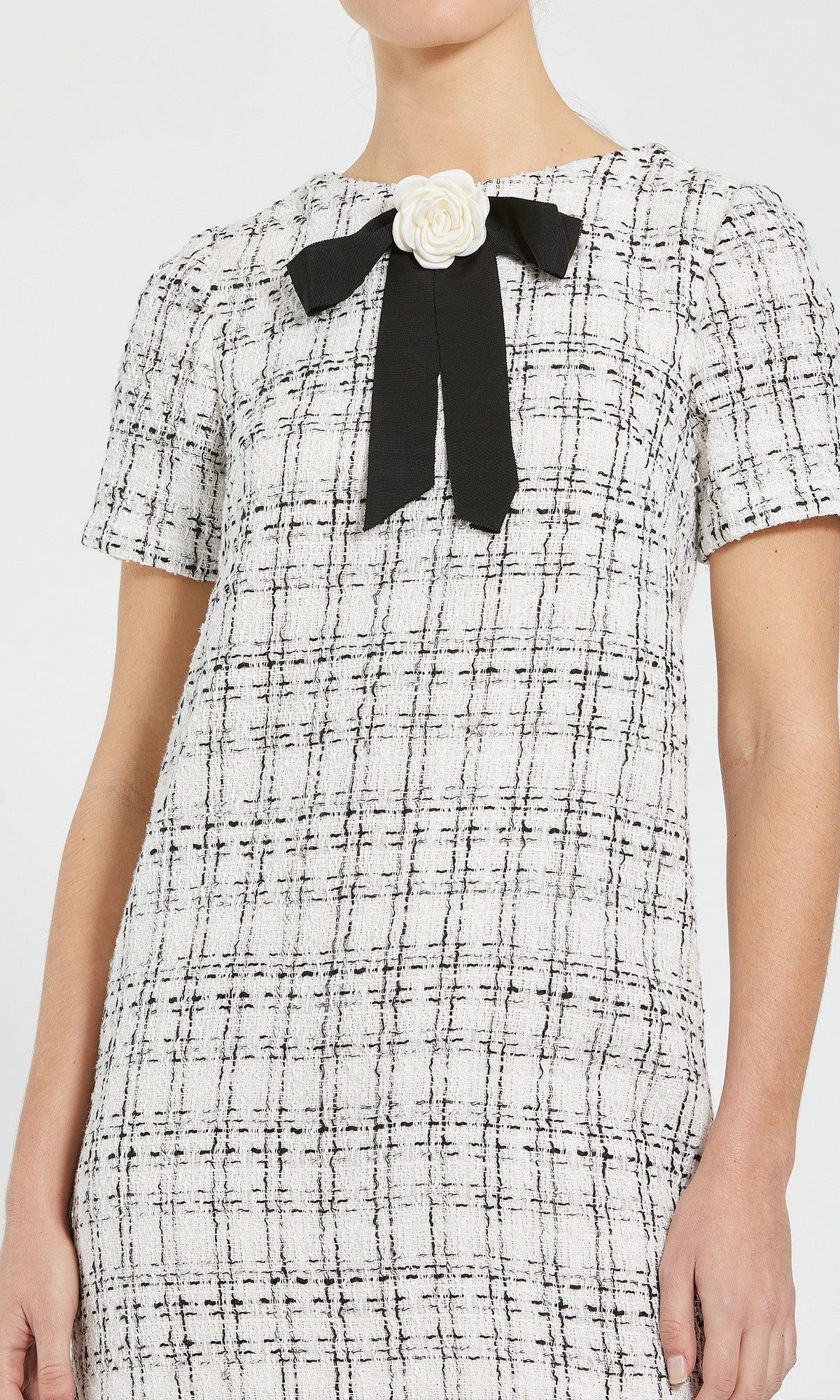 A woman wearing the Mac Duggal 27796 short semi-formal dress, featuring short sleeves, a black-and-white plaid pattern, and chic details like a black ribbon with a white flower accent at the collar—reminiscent of a stylish black bow mini dress.